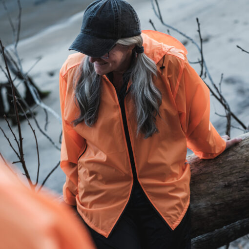 Woman sitting on a log wearing AntiGravtiyGear Blaze Orange Rain Jacket